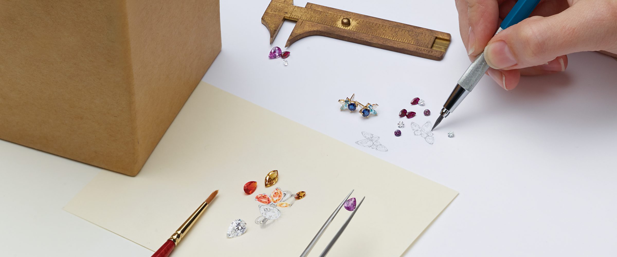 Jeweler sketching a custom jewelry design with loose gemstones and finished gold earrings